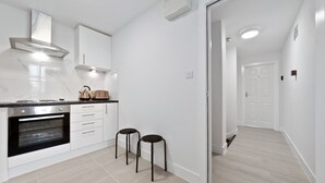 A modern kitchen with white cabinetry, a built-in oven, and two black stools. - Serviced Ensuite Room Crystal Palace London Se20 (London)