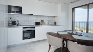 A modern kitchen with white cabinetry, a built-in oven, and a dining area with a wooden table and chairs. - Porto Ocean Flat (Vila Nova de Gaia)