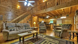 A spacious living area with a high ceiling, wooden beams, a sofa set, a coffee table, and a patterned rug. - Welcome to Relaxing River Retreat, where your pets are welcome amidst a scenic riverfront, screened porch, hot tub, WiFi, firepit, and abundant wildlife (Ellijay)