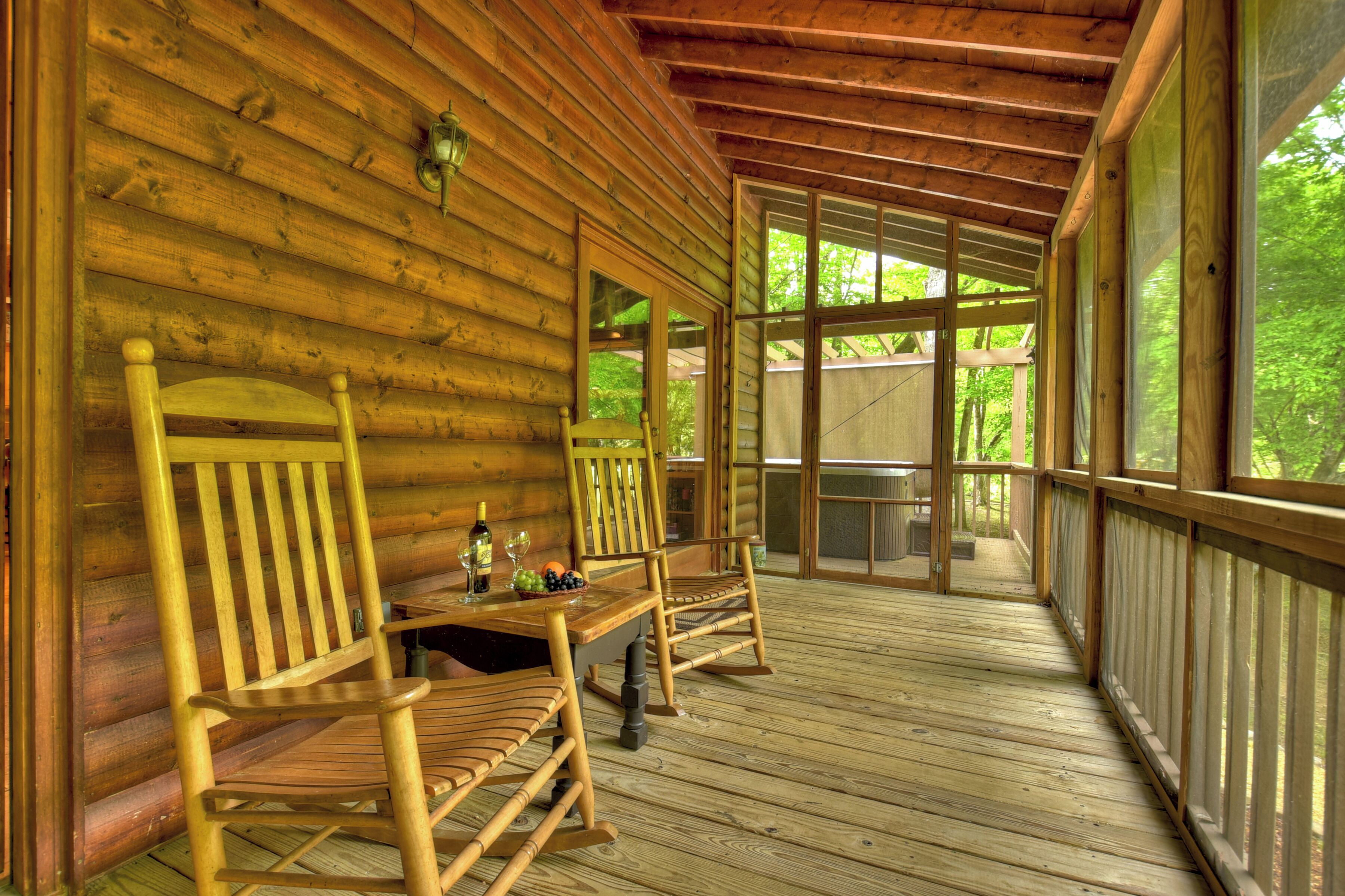 A wooden deck with rocking chairs and a table, overlooking a forest.