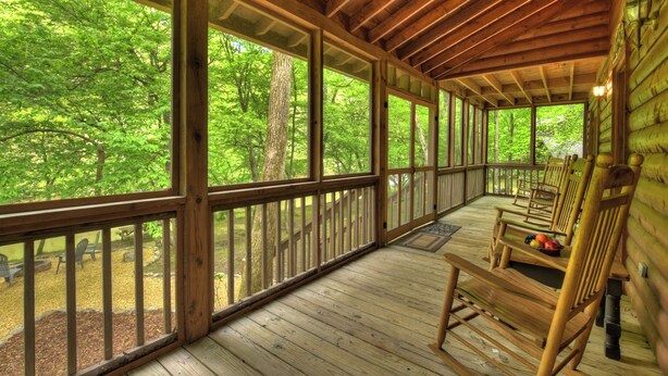 A covered wooden deck with large windows, wooden railings, and several rocking chairs. - Welcome to Relaxing River Retreat, where your pets are welcome amidst a scenic riverfront, screened porch, hot tub, WiFi, firepit, and abundant wildlife (Ellijay)