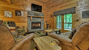 A cozy cabin interior with a stone fireplace, leather furniture, and wooden walls. - Welcome to Relaxing River Retreat, where your pets are welcome amidst a scenic riverfront, screened porch, hot tub, WiFi, firepit, and abundant wildlife (Ellijay)