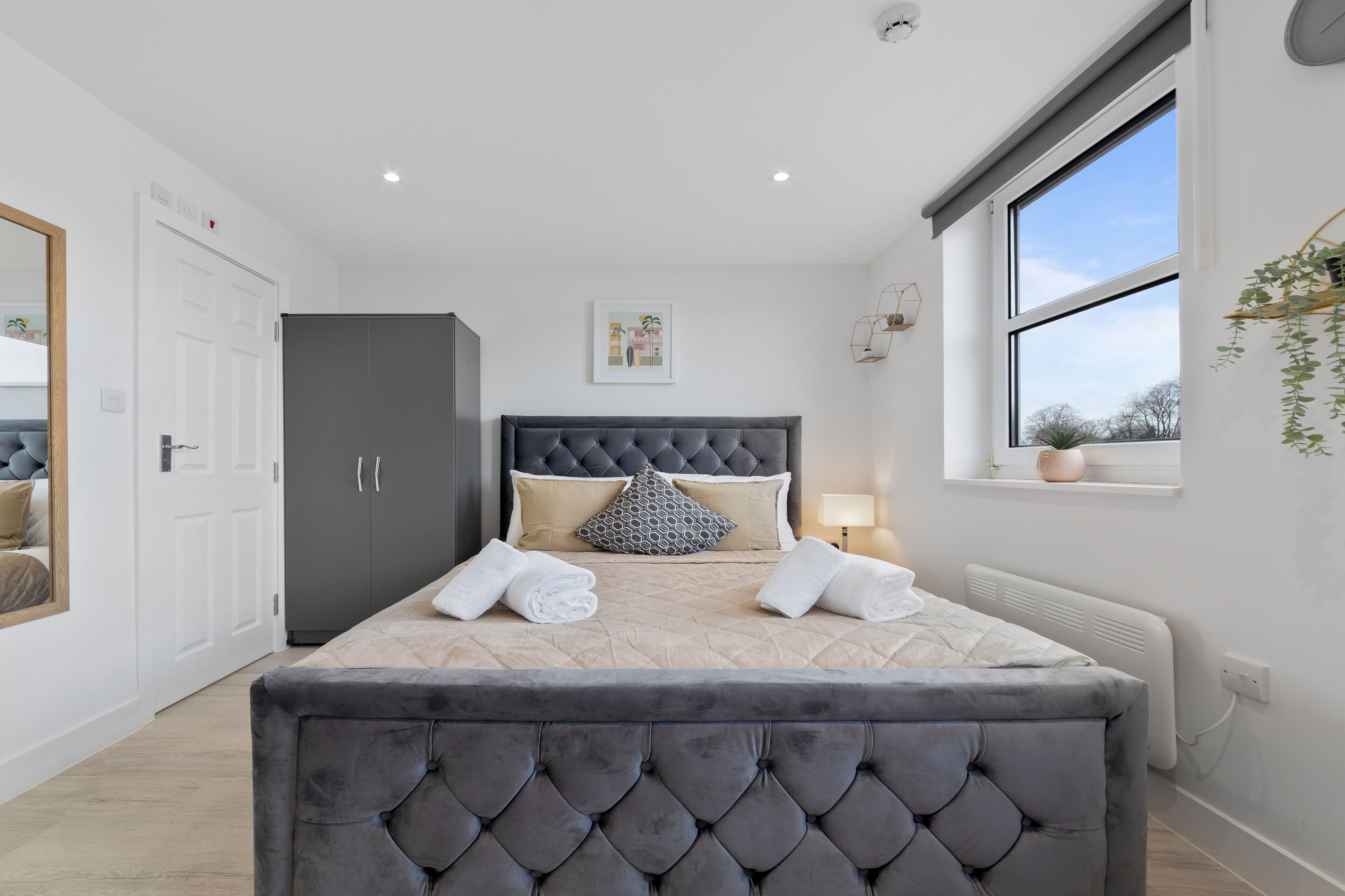 A bedroom with a large bed, a wardrobe, a window with a view, and a bedside table with a lamp.
