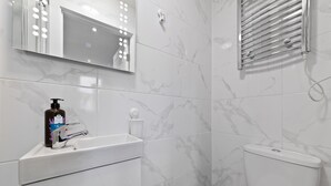 Ein Badezimmer mit einem weißen Waschbecken, einem beleuchteten Spiegel, einer Toilette und einer Duschkabine.