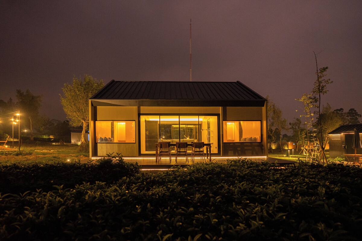 Een modern, lichtrijk huis met een groot raam, omringd door een tuin.