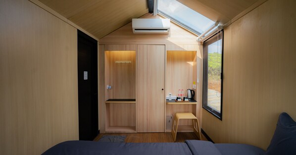 A compact room with a bed, a small table with a kettle, and a window.