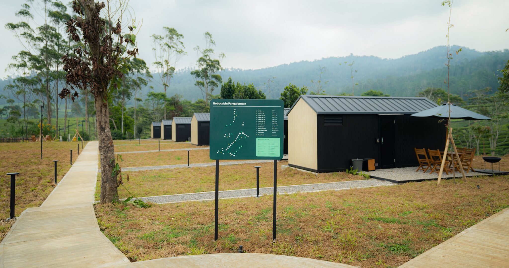 A campsite with a map sign, cabins, and a dining area.