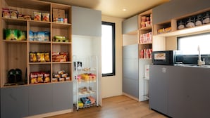 A compact kitchen with shelves stocked with snacks, a refrigerator, and a microwave.