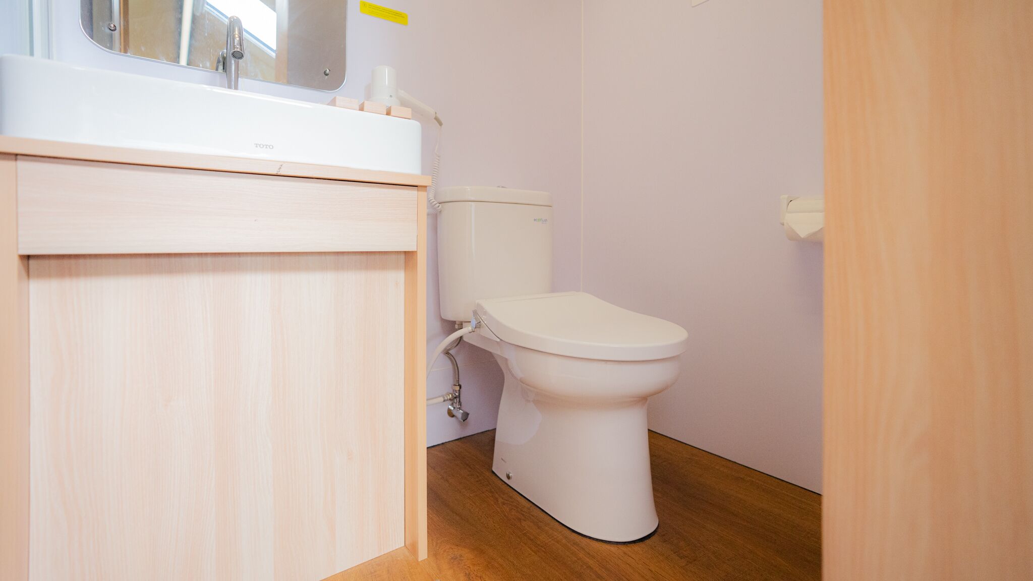 Une petite salle de bain propre, avec des toilettes blanches, un lavabo et un miroir.