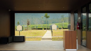 A modern hotel lobby with a large glass door leading to a scenic view of tea fields and buildings.