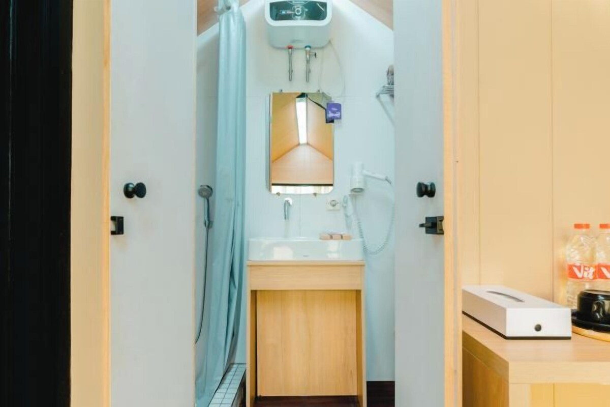 A narrow hallway leading to a bathroom with a sink, a mirror, and a shower. There is a towel rack and a small cabinet on the wall.
