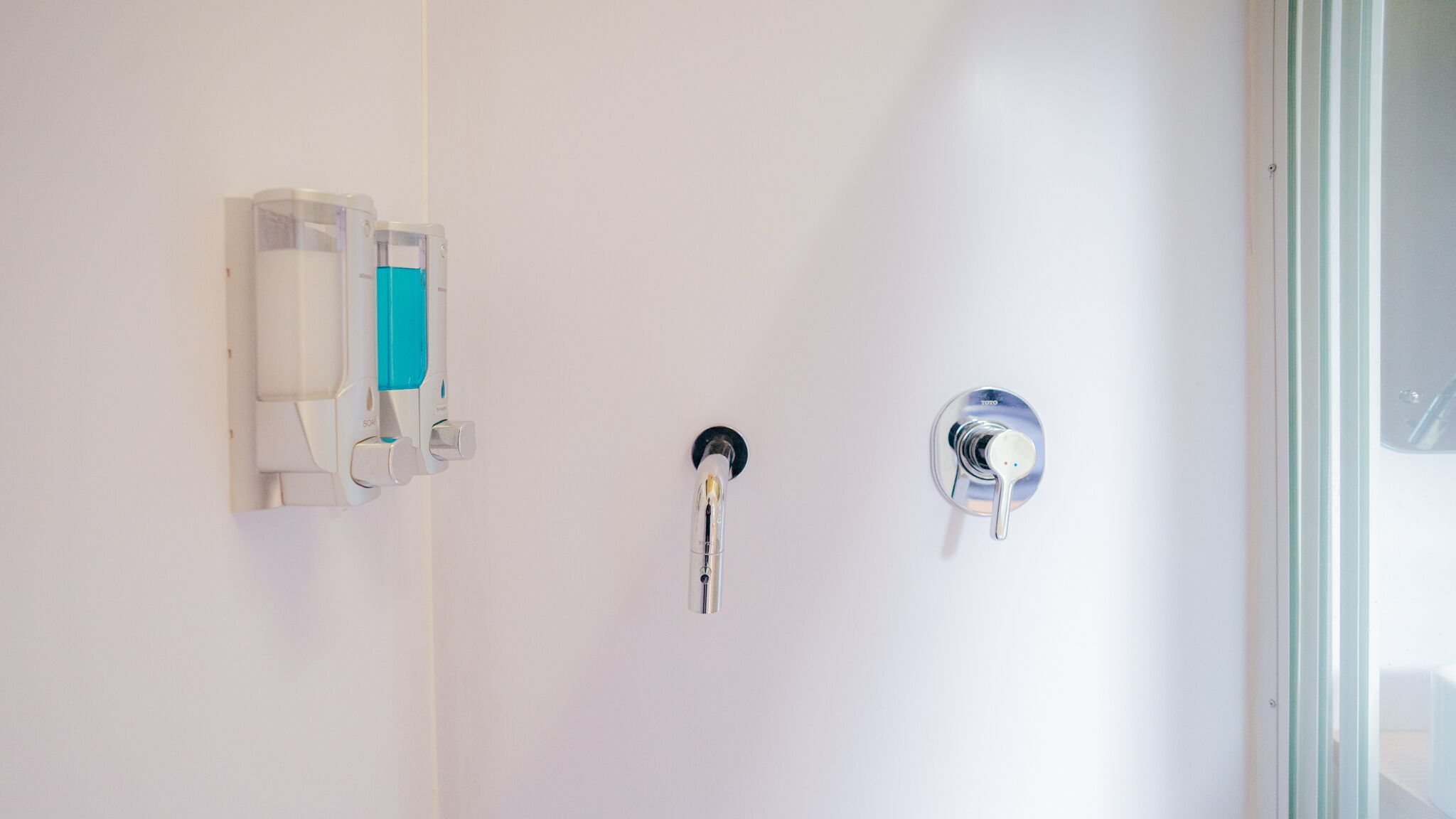 Ein Badezimmer mit Handtrockner, Handtuchspender und einer Duscharmatur.