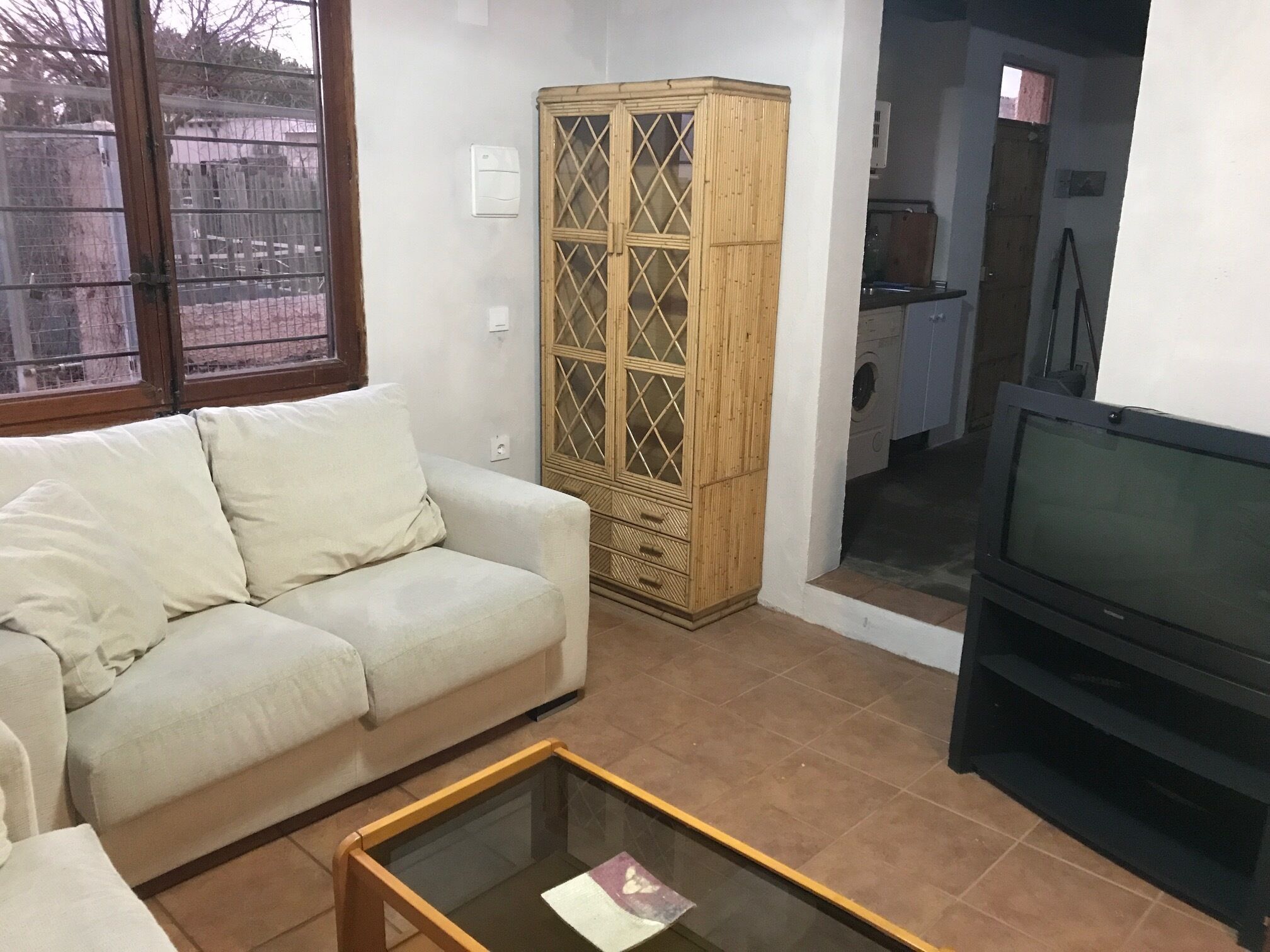 Un salon avec un canapé beige, une table basse en verre, un meuble en bois et un téléviseur.