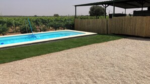 Une piscine dotée d’une terrasse en bois et d’une pergola, entourée d’une clôture et bordée, au loin, par un vignoble.