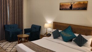 A hotel room with a large bed, two armchairs, a small table, a nightstand with a lamp, and a ceiling fan. - Wild Pensione Resort  (Ramnagar)