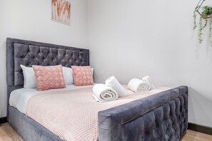 A neatly made bed with a tufted headboard, pink and white pillows, and rolled towels on a pink textured bedspread. - Serviced Ensuite Room Studio Sydenham London Se26 (London)