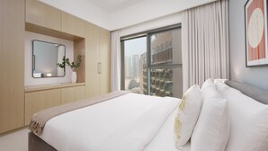 A modern hotel room with a large bed, a bedside table with a vase, a mirror, and a window with curtains. - Maison Privee - Modern Chic Apt w/ Unobstructed Burj Khalifa Views (Dubai)