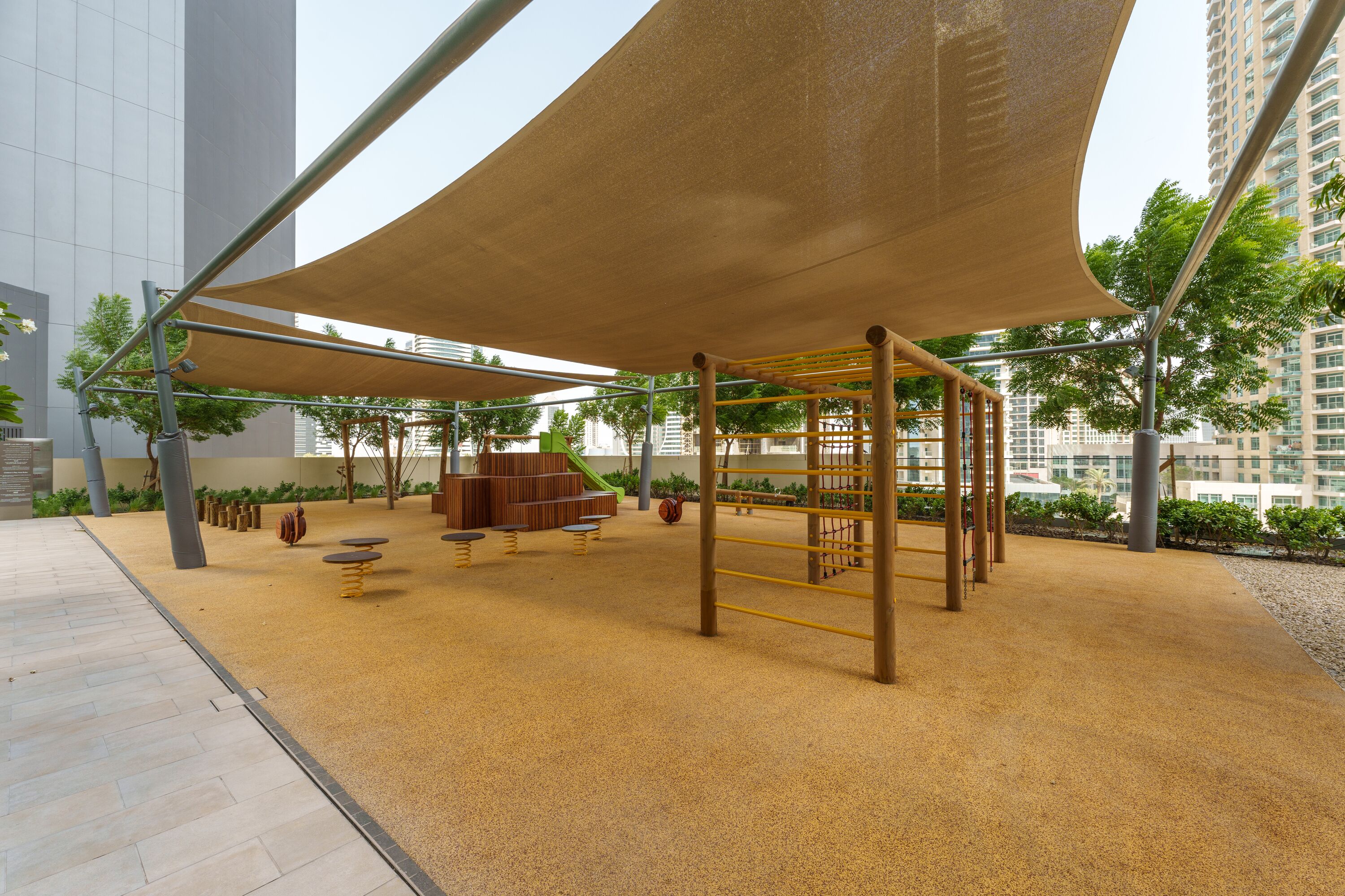 Een buitenspeeltuin met klimconstructies en zachte speelzones, gelegen in een moderne stedelijke omgeving.
