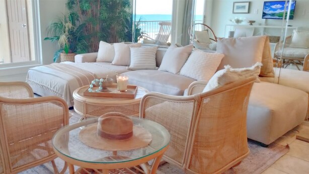 A cozy living room with a sofa, two armchairs, a glass coffee table, and a wicker chair.
