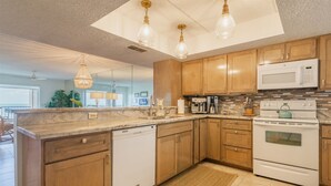 A modern kitchen with wooden cabinets, a built-in dishwasher, a stove, and a microwave. There are pendant lights and a chandelier.