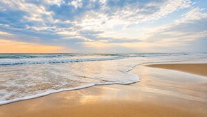 A beach with waves, a clear sky, and a sunset.