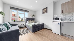 A modern bedroom with a bed, a grey sofa, and a small kitchenette with a microwave. - Cozy Serviced En-suite Room Sydenham London Se26 (London)