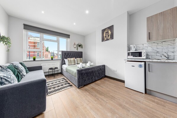 A modern bedroom with a bed, a grey sofa, and a small kitchenette with a microwave.