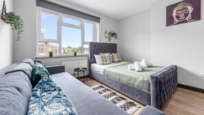 A modern bedroom with a bed, a sofa, a small table, and a window with a view of buildings. - Cozy Serviced En-suite Room Sydenham London Se26 (London)