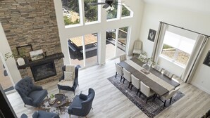 Un amplio salón con chimenea de piedra, ventanas grandes y una zona de comedor con una mesa larga y sillas.