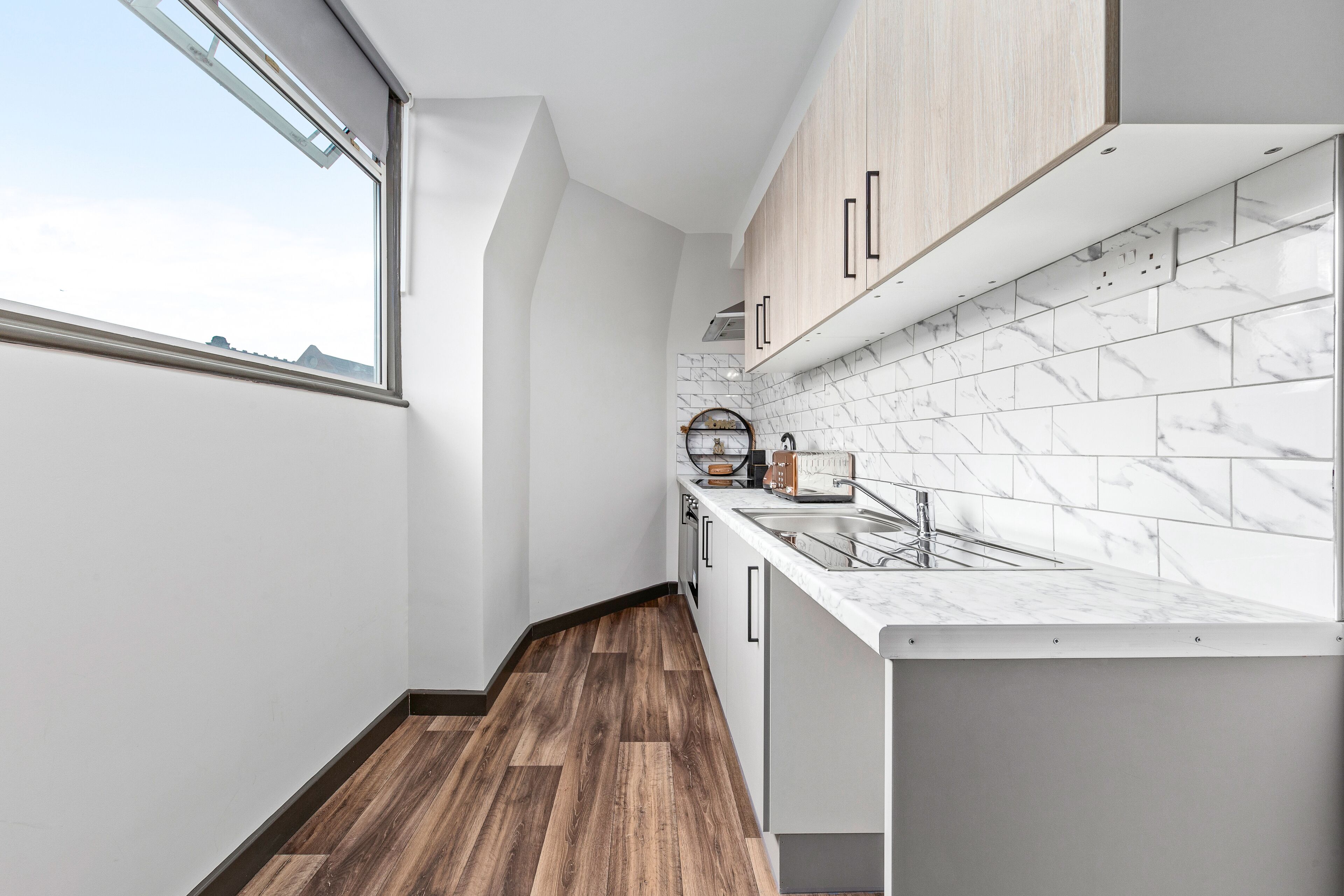 Une cuisine moderne avec des carreaux de marbre blanc, des armoires en bois et une fenêtre qui laisse entrer la lumière naturelle.