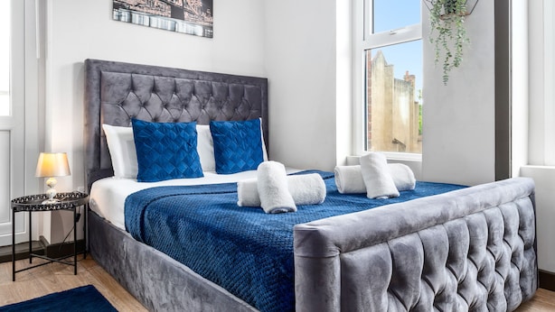 A bedroom with a tufted headboard, a bed with blue and white bedding, a blue throw blanket, and a hanging plant. - Sleep 4 Serviced Ensuite Room Sydenham London Se26 (London)