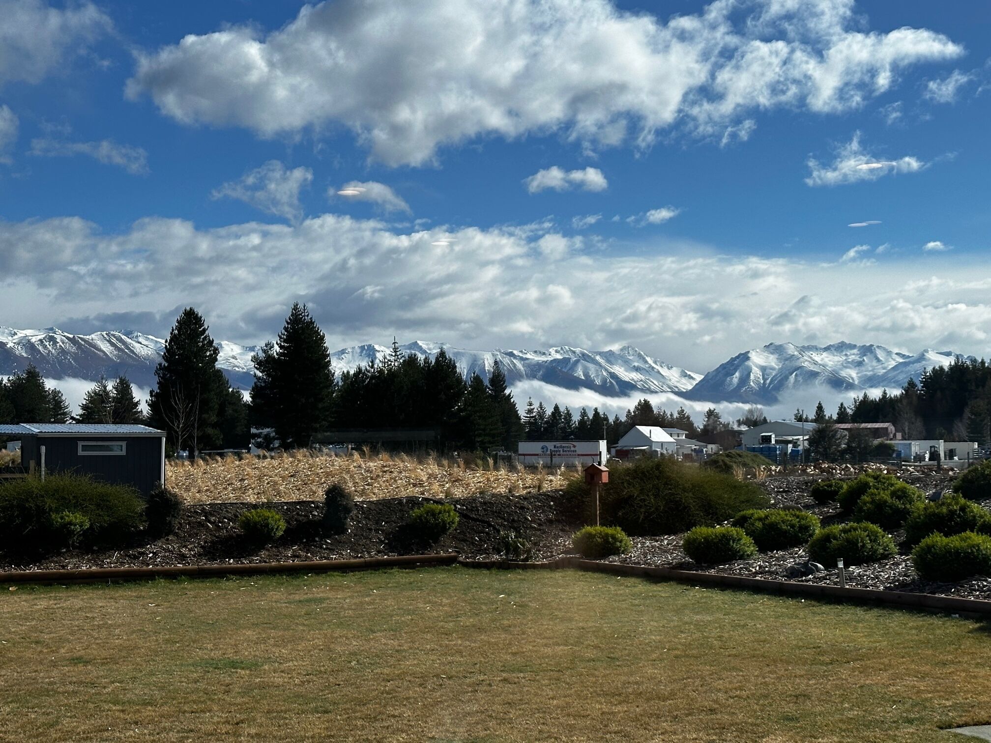 Blick auf eine Berglandschaft mit schneebedeckten Gipfeln, blauem Himmel und einem kleinen Gebäude mit einem Schild im Vordergrund.