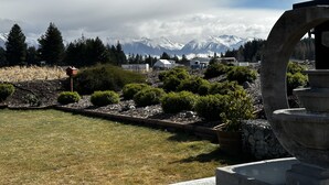 A garden with a stone fountain, a wooden birdhouse, and a view of snow-capped mountains in the background.