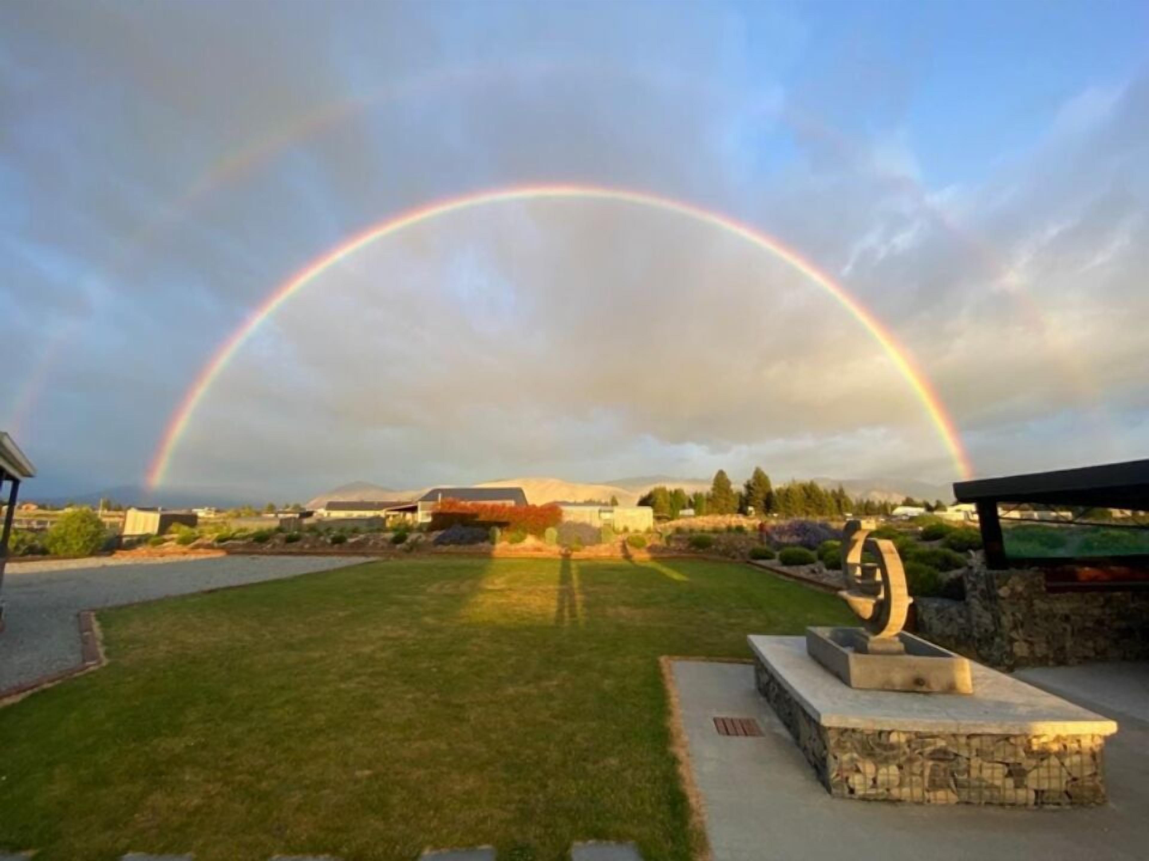 A park with a stone sculpture, a grassy area, and a rainbow in the background.