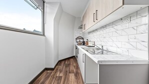 A modern kitchen with white marble tiles, wooden cabinets, and a window providing natural light.