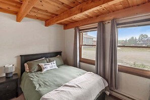 A bedroom with a bed, a nightstand, a window with curtains, and a view of the outside. - Riverbend Retreat-Pet friendly and amazing views (Crested Butte)