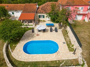 Piscina com ladrilhos de pedra, cercada por um muro de pedra, e área de pátio com móveis para área externa.