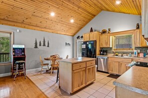 A kitchen with wooden cabinets, a refrigerator, a dishwasher, and a dining area with chairs and a table. - Great location! 2BR w/Hot Tub + Firepit + Grill (Sevierville)