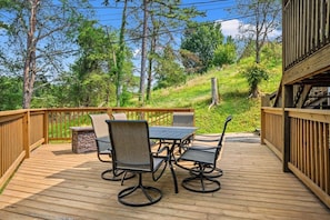 A wooden deck with a table and chairs, surrounded by a wooden railing, overlooking a grassy area with trees. - Great location! 2BR w/Hot Tub + Firepit + Grill (Sevierville)