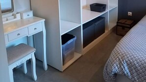 A bedroom with a bed, a white desk with drawers, a chair, a wardrobe with shelves, and a small bedside table. - Appartement en Aveyron (Aubin)