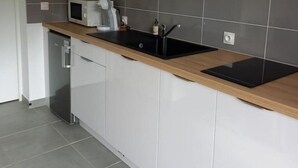 A modern kitchen with grey tiles, a wooden countertop, a built-in microwave, and a wall-mounted clock. - Appartement en Aveyron (Aubin)