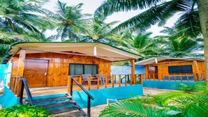 A wooden bungalow with a covered porch, a screened porch, and a staircase leading to the entrance. - Dersy Beach Resort (Canacona)