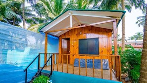 A wooden cabin with a covered porch, a screened window, and a staircase leading to the entrance. - Dersy Beach Resort (Canacona)