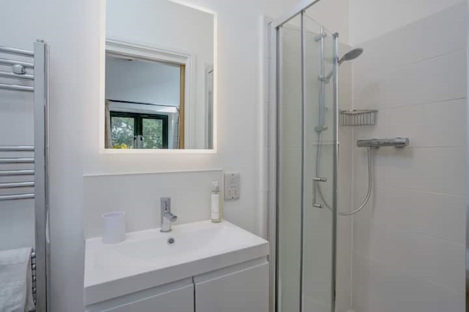 A modern bathroom with a glass-enclosed shower, a white sink, and a window above the mirror.