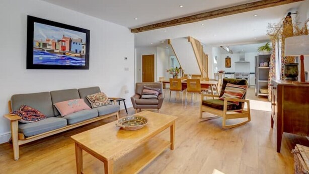 A spacious living area with a sofa, coffee table, and dining table. A painting is on the wall, and the room has wooden flooring and a high ceiling.