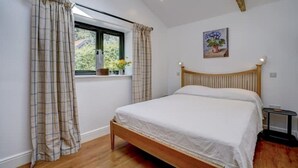 A bedroom with a wooden bed, plaid curtains, a window with a view of greenery, and a painting on the wall.