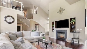 Una sala de estar amplia con un sofá grande, una chimenea, un televisor y una escalera que sube a un nivel superior.