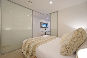 Un dormitorio moderno con una cama grande, un armario de puertas de cristal, un escritorio con silla y un televisor montado en la pared.