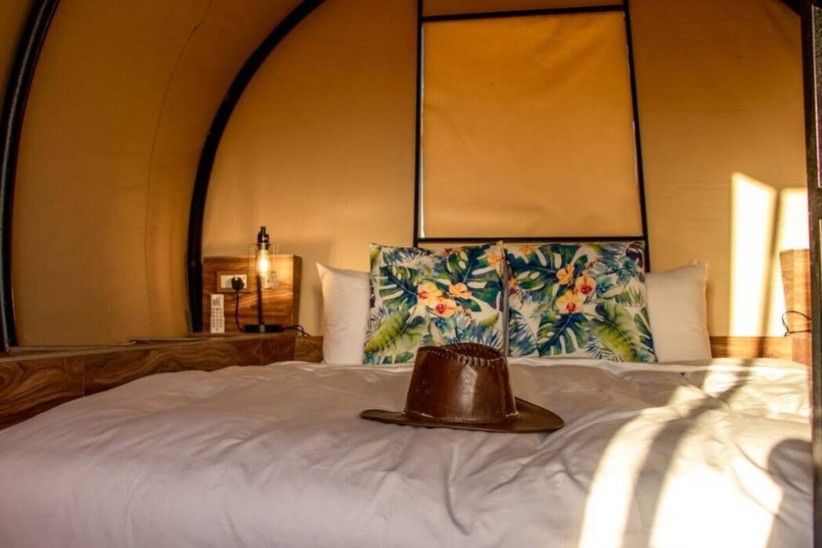 A tent-style room with a bed, a hat on the bed, and a floral wall hanging.