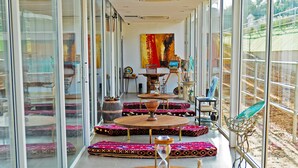 A spacious room with large windows, a central seating area with patterned cushions, and a view of the outdoors. - NIRVANA RETREAT (Ras Al Khaimah)